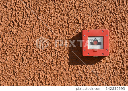 Red fire alarm manual call point on a textured orange wall Red fire alarm manual call point on a textured orange wall 142839693