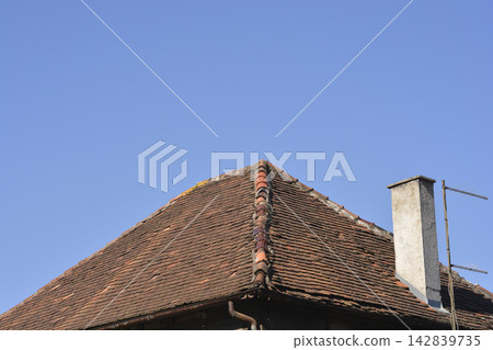 Old clay tile roof with a concrete chimney against a blue sky 142839735