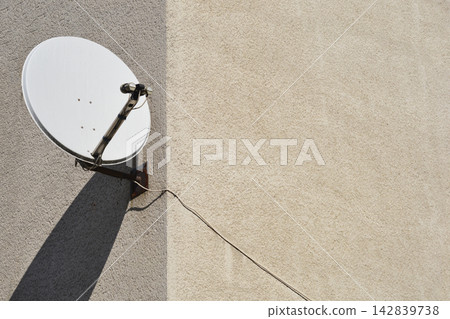 White satellite dish mounted on a textured building wall White satellite dish mounted on a textured building wall 142839738