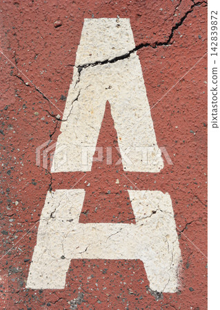 White letter A painted on cracked red asphalt ground in a vertical view White letter A painted on cracked red asphalt ground in a vertical view 142839872