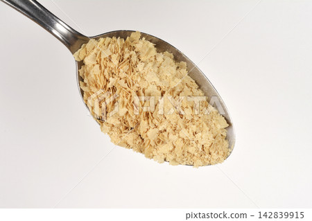 Nutritional yeast flakes on a metal spoon isolated on a white background 142839915