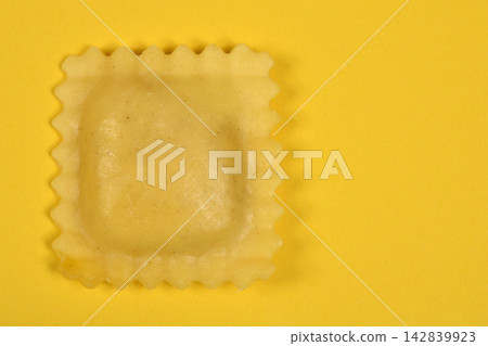 Single ravioli pasta piece on yellow background Single ravioli pasta piece on yellow background 142839923