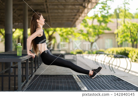 Fit young woman doing back push ups and looking focused and involved Fit young woman doing back push ups and looking focused and involved 142840145