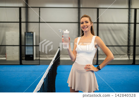 Cute caucasian young woman at paddle tennis court with a bottle of water in hands Cute caucasian young woman at paddle tennis court with a bottle of water in hands 142840328