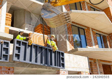 Builders guiding suspended metal panel lifted by excavator bucket Builders guiding suspended metal panel lifted by excavator bucket 142840503