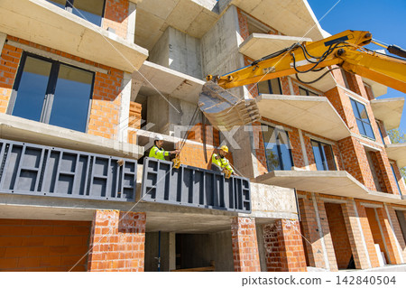 Excavator lifting metal panel near multi story building frame 142840504