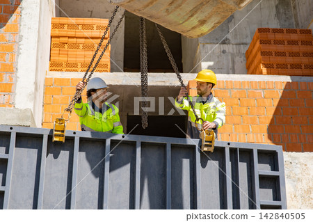 Two male builders adjusting chains on steel formwork panel Two male builders adjusting chains on steel formwork panel 142840505