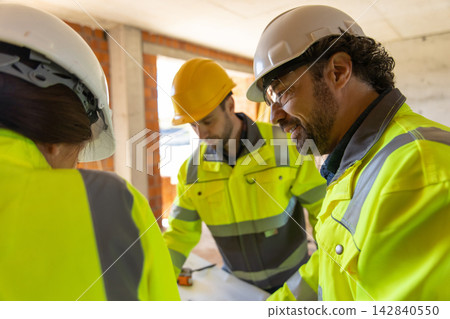 Smiling civil engineer inspecting blueprints with colleagues Smiling civil engineer inspecting blueprints with colleagues 142840550