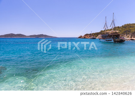 Blue sea laps a sandy shore beside rocky cliffs where. Turkey Blue sea laps a sandy shore beside rocky cliffs where. Turkey 142840626