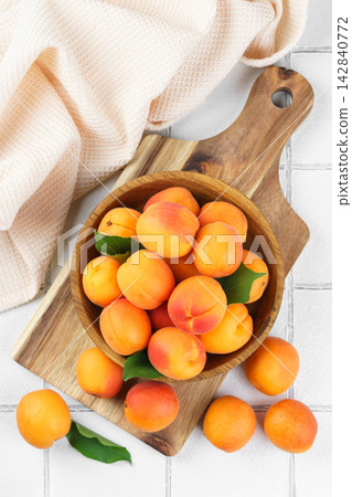Fresh ripe apricots fruits in wooden bowl on white tile background. healthy eating, food ingredient Fresh ripe apricots fruits in wooden bowl on white tile background. healthy eating, food ingredient 142840772