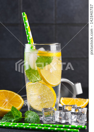 Fresh homemade lemonade with lemon slices, mint and ice in glasses on black kitchen tile background Fresh homemade lemonade with lemon slices, mint and ice in glasses on black kitchen tile background 142840787