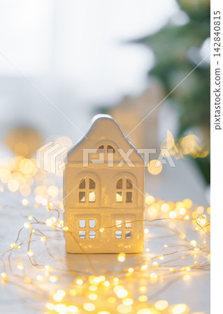 Minimalist Christmas decor, ceramic house on garland warm festive fairy lights background Minimalist Christmas decor, ceramic house on garland warm festive fairy lights background 142840815