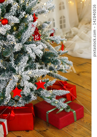 Frosted Christmas tree decorated with red stars, red baubles and warm fairy lights, wrapped presents Frosted Christmas tree decorated with red stars, red baubles and warm fairy lights, wrapped presents 142840816