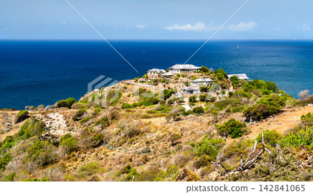 Coastal villas and houses on a sunny green hilltop overlooking Windward Bay and the deep blue ocean in Antigua and Barbuda. Coastal villas and houses on a sunny green hilltop overlooking Windward Bay and the deep blue ocean in Antigua and Barbuda. 142841065