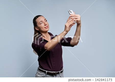 Young female student taking selfie with smartphone studio portrait grey background Young female student taking selfie with smartphone studio portrait grey background 142841173