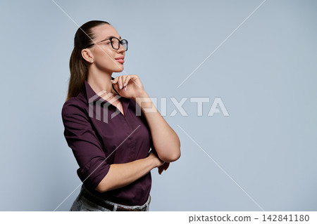 Young woman in glasses thinking with hand on chin looking aside Young woman in glasses thinking with hand on chin looking aside 142841180