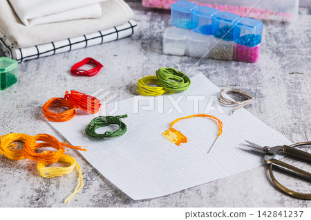 Cross-stitch, Aida cloth, colorful embroidery floss, and scissors on the table. Cross-stitch, Aida cloth, colorful embroidery floss, and scissors on the table. 142841237