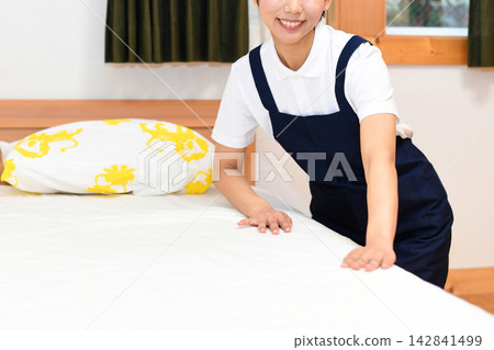 一位微笑的客房服務人員正在鋪床。 一位微笑的客房服務人員正在鋪床。 142841499