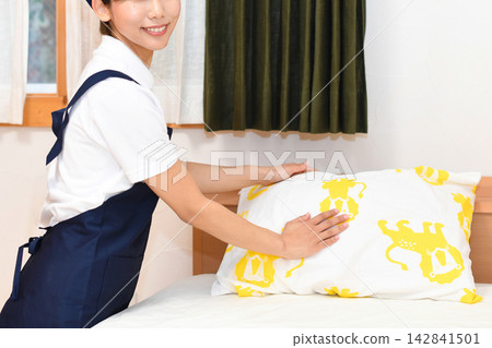 一位微笑的客房服務人員正在鋪床。 一位微笑的客房服務人員正在鋪床。 142841501