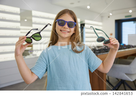 Charming girl tests fashionable sunglasses inside store Charming girl tests fashionable sunglasses inside store 142841653
