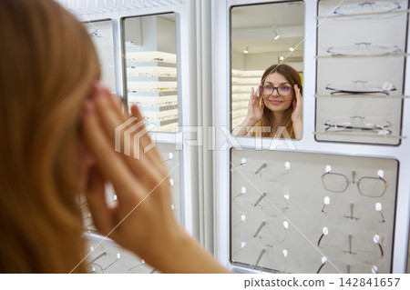 Woman customer smiles while fitting new eyeglasses in boutique Woman customer smiles while fitting new eyeglasses in boutique 142841657