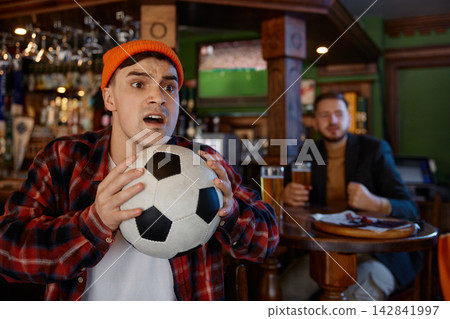 Excited supporter gazes at television. Enthusiastic fan observes match with focus and excitement Excited supporter gazes at television. Enthusiastic fan observes match with focus and excitement 142841997