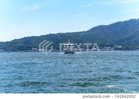 The Miyajima ferry sails across the calm Seto Inland Sea, with the lush green mountains on the opposite shore in the background. The Miyajima ferry sails across the calm Seto Inland Sea, with the lush green mountains on the opposite shore in the background. 142842002
