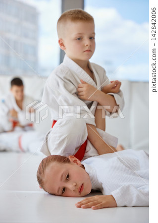 Children competing and cooperating in martial arts practice within lively indoor dojo environment Children competing and cooperating in martial arts practice within lively indoor dojo environment 142842006