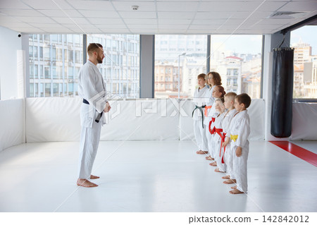 Trainer provides instruction on correct manners during practice session of martial arts for children Trainer provides instruction on correct manners during practice session of martial arts for children 142842012