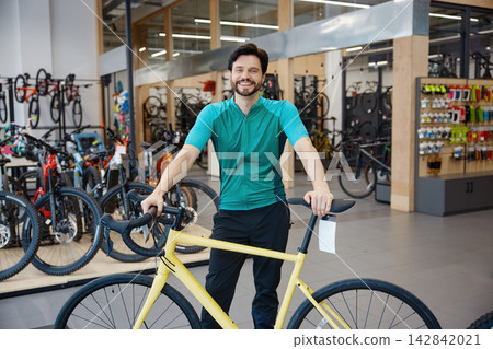 Enthusiastic salesperson showcasing bicycle for test ride amidst well-stocked store environment Enthusiastic salesperson showcasing bicycle for test ride amidst well-stocked store environment 142842021