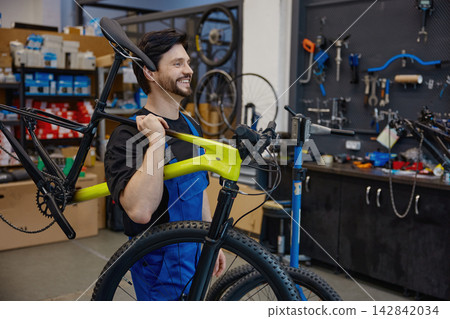 Skilled mechanic smiling while analyzing bicycle components in busy workshop environment Skilled mechanic smiling while analyzing bicycle components in busy workshop environment 142842034