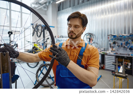 Professional worker adjusting bike wheel in busy workshop setting Professional worker adjusting bike wheel in busy workshop setting 142842036