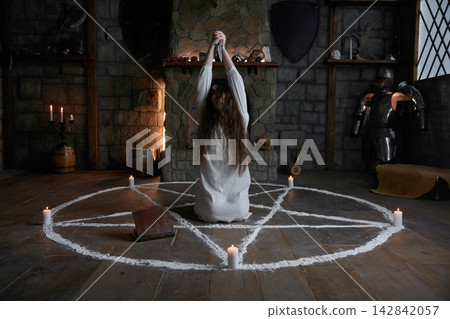 Young female spellcaster in engraved stone chamber carries out intense mystical ritual Young female spellcaster in engraved stone chamber carries out intense mystical ritual 142842057