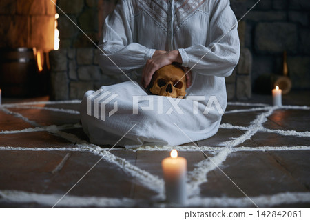 Crop of woman in ceremonial attire practicing exorcism reverent rituals amidst candlelit surrounding 142842061