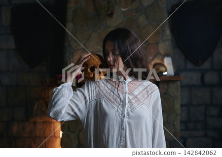 Woman gently grasping skull amidst candlelit stone setting for contemplative study. Exorcism ritual Woman gently grasping skull amidst candlelit stone setting for contemplative study. Exorcism ritual 142842062
