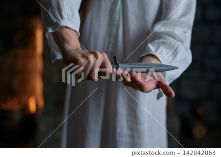 Hands holding dagger against palm nightgown hearth glow, tense ritual inspection Hands holding dagger against palm nightgown hearth glow, tense ritual inspection 142842063