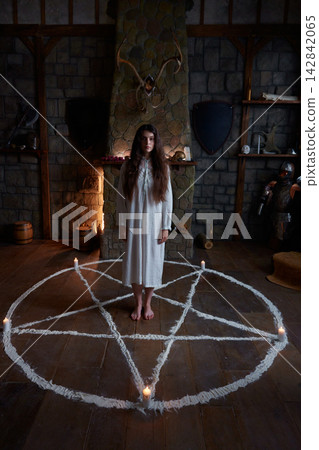 Caucasian woman standing inside exorcism pentagram circle, candlelit medieval chamber Caucasian woman standing inside exorcism pentagram circle, candlelit medieval chamber 142842065