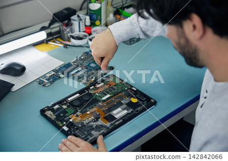 A man is working on a motherboard with a magnifying glass 142842066