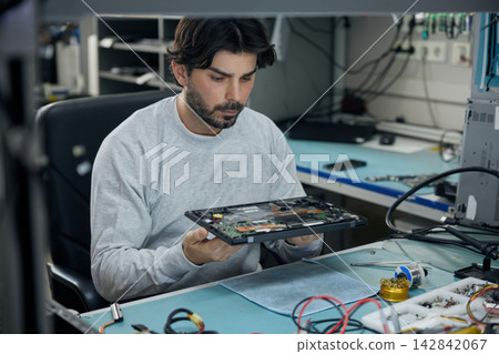 A man at a desk is carefully examining a motherboard A man at a desk is carefully examining a motherboard 142842067