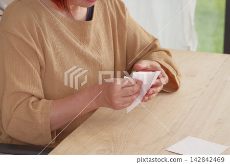 A senior woman folds origami at a nursing home. A senior woman folds origami at a nursing home. 142842469