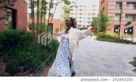 A young woman relaxes and unwinds while walking along a city street in a new eco-friendly residential complex. She dances to background music and laughs. Concept of relaxation and stress-free A young woman relaxes and unwinds while walking along a city street in a new eco-friendly residential complex. She dances to background music and laughs. Concept of relaxation and stress-free 142843183