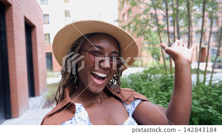 Happy attractive young girl smiling and looking at camera taking selfie. Cute woman broadcasting video from smartphone, waving hand towards webcam. She records vlog, broadcasts for social networks Happy attractive young girl smiling and looking at camera taking selfie. Cute woman broadcasting video from smartphone, waving hand towards webcam. She records vlog, broadcasts for social networks 142843184
