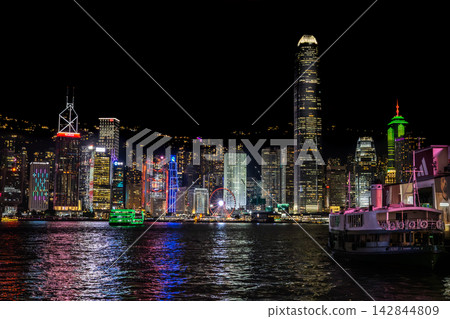 香港維多利亞港的摩天大樓在夜色中熠熠生輝,倒映在水面上。 香港維多利亞港的摩天大樓在夜色中熠熠生輝,倒映在水面上。 142844809