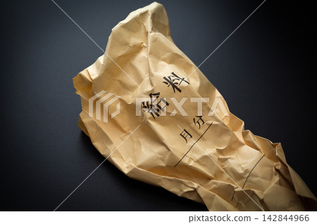 A crumpled pay envelope in a black background. A crumpled pay envelope in a black background. 142844966