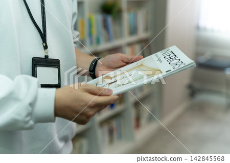 辦公室裡一名員工拿著一本《室內設計》雜誌工作。 辦公室裡一名員工拿著一本《室內設計》雜誌工作。 142845568