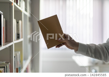 Close-up of a man's hands as he takes a book from a bookshelf. Close-up of a man's hands as he takes a book from a bookshelf. 142845585