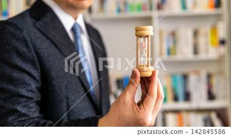 A man in a suit holding an hourglass A man in a suit holding an hourglass 142845586