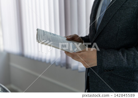 一名身穿西裝的男子手持報紙,正在查看新聞。 一名身穿西裝的男子手持報紙,正在查看新聞。 142845589