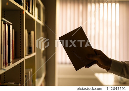 一隻男人的手從書架上拿起一本書。 142845591