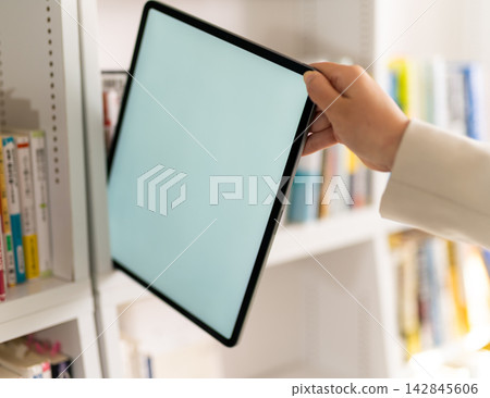 A business person's hand takes a tablet from a bookshelf. A business person's hand takes a tablet from a bookshelf. 142845606